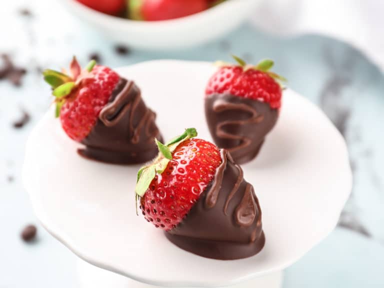 Dessert stand with delicious strawberries dipped in dark chocolate on color background