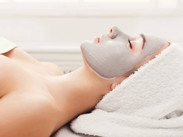 Face mask, spa beauty treatment. Woman applying facial clay mask at spa salon, skincare, side vies