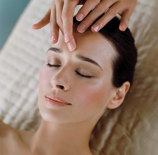 Close up of brown haired woman lying down having facial to forehead with eyes closed. spa treatments