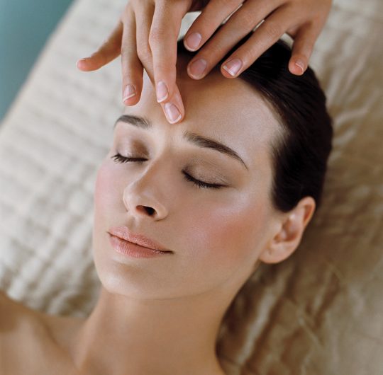 Close up of brown haired woman lying down having facial to forehead with eyes closed. spa treatments